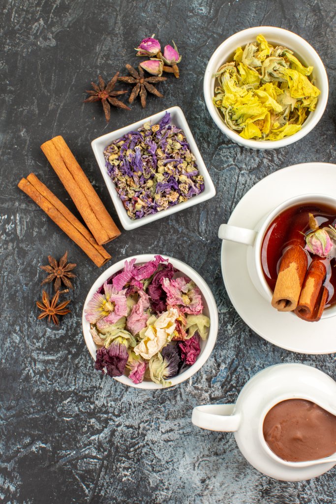 a cup of herba tea with different dry flowers and melted chocolate on grey background