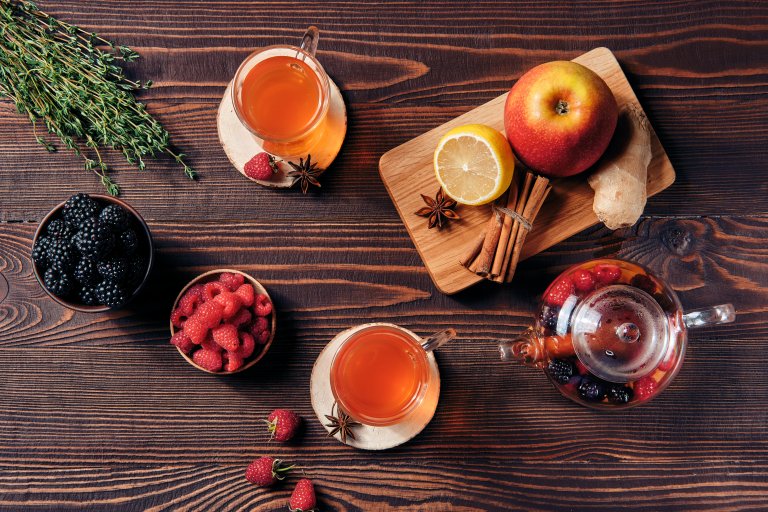 Fruit tea with raspberries, bramble, apple and lemon in cups and teapot