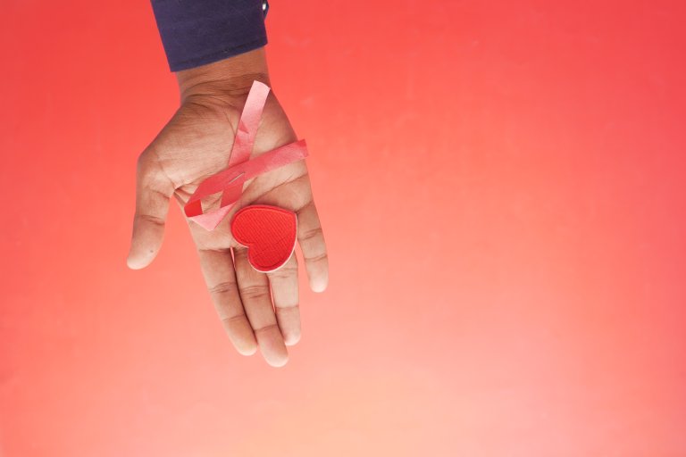 hand holding red HIV ribbon top down