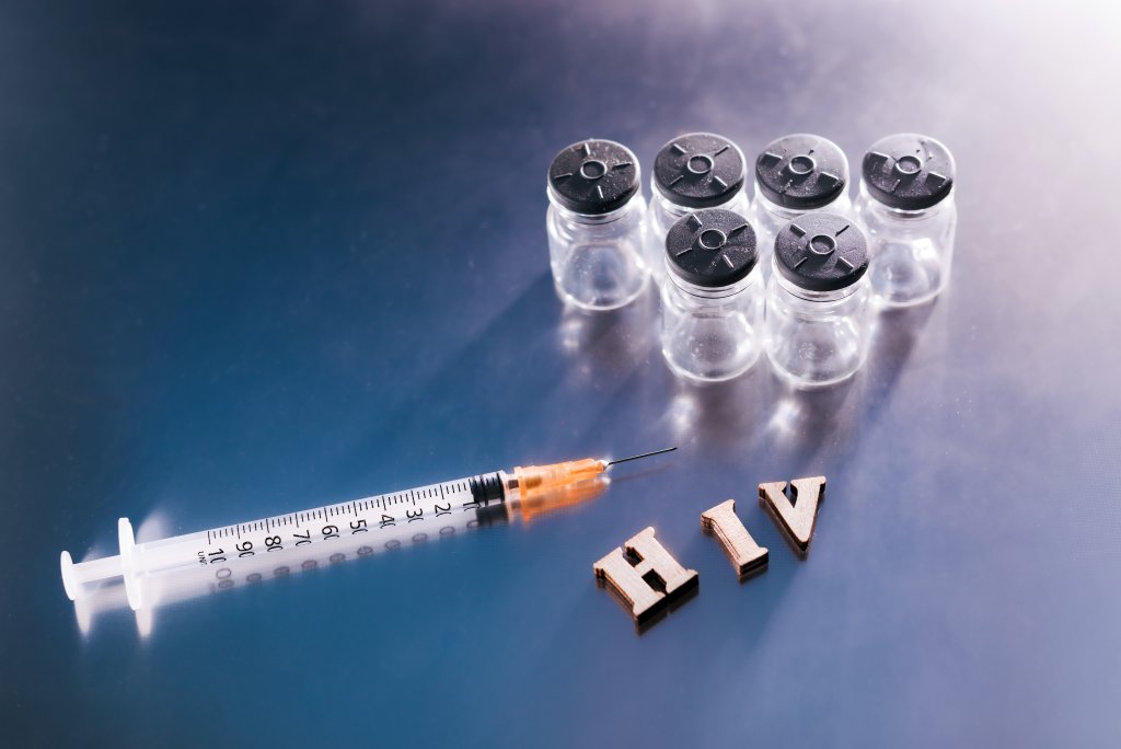New AIDS treatment, vaccination with syringe with new vaccine, letters HIV on medical background.
