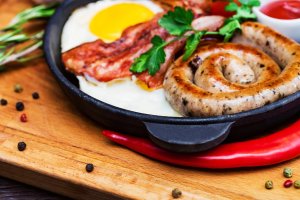 Nutritious meal with fried egg, sausage, bacon, tomato and sauce in frying pan