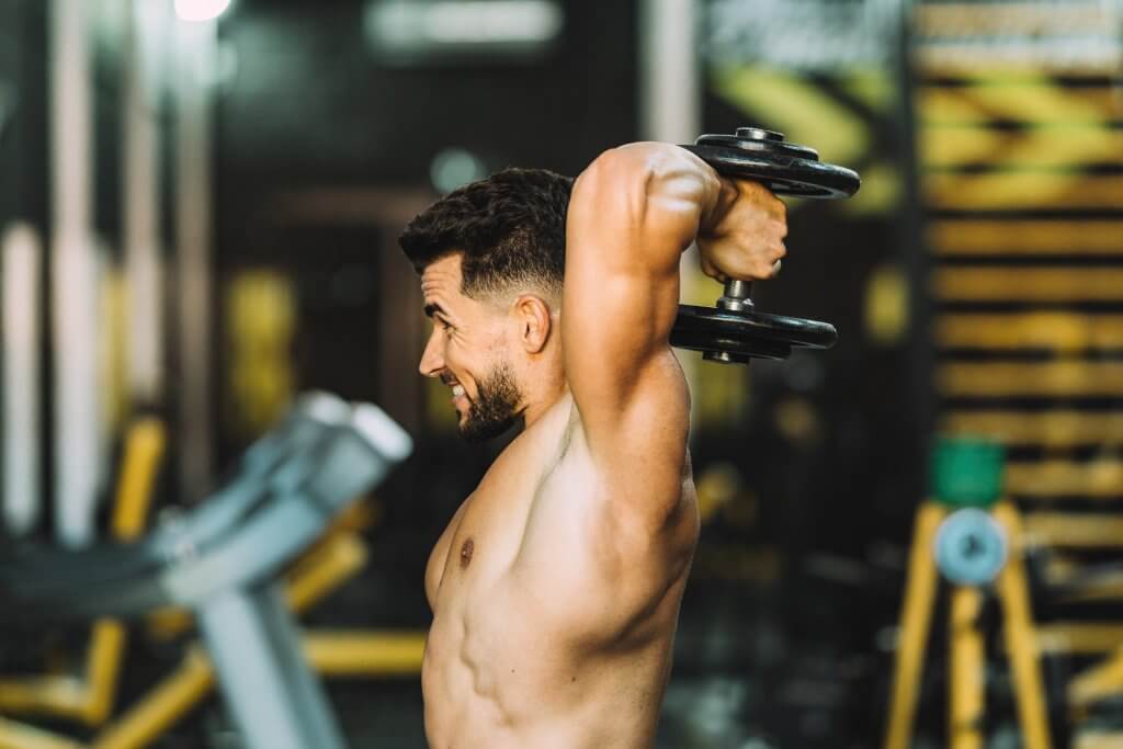 Profile of a strong man exercising with weights in a gym