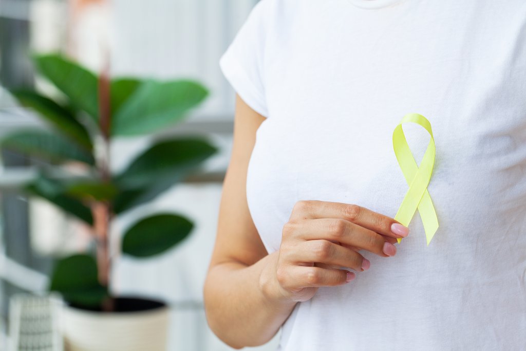 Woman in white t-shirt holding and showing yellow awareness ribbon in her hands