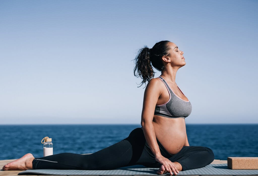 Pregnant woman doing yoga exercise routine next to the beach