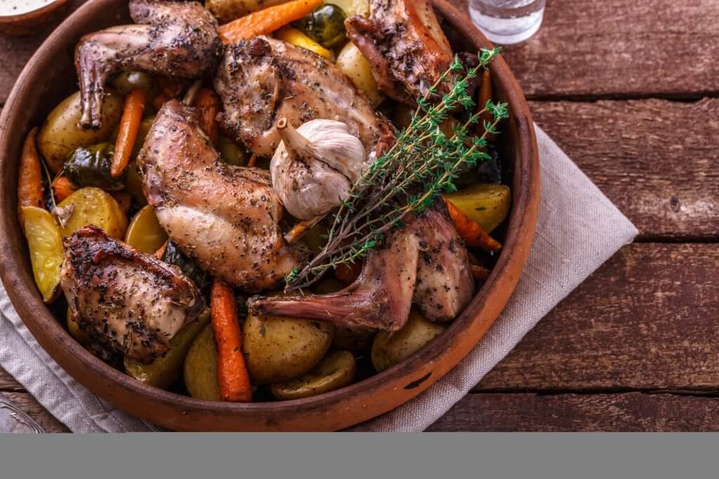 Oven baked rabbit with root vegetables and herbs, rustic style