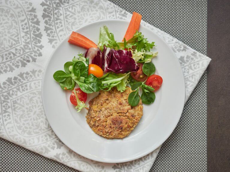 chickpea veggie burger and salad on a white plate on a gray tablecloth and napkin, view from above